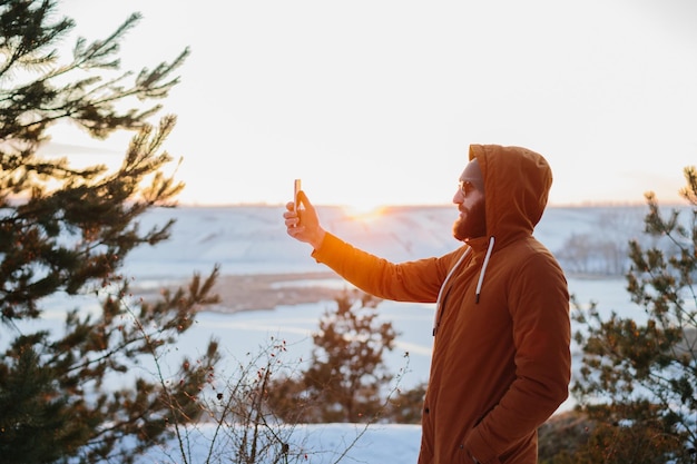 A hiker enjoys the sunset in the winter mountains and takes a photo on his phone