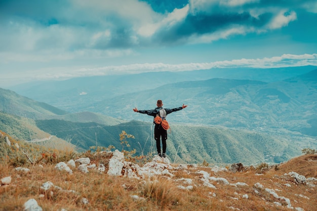 Hiker man with backpack standing on the top mountain cliff