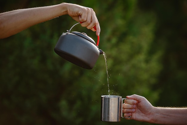 Hiker pouring a hot drink from a metal teapot into a steel mug