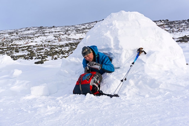 Hiker pours himself a tea from a thermos sitting in a snowy house igloo