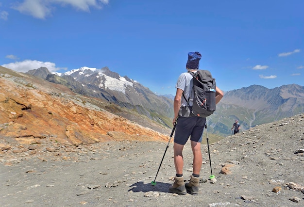 A hiker standing on the trail of the tour of Mont Blanc in summer znd looking the glaciers far away