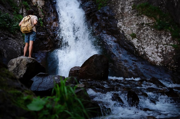 Hiker waalkinh with backpack looking at waterfall in park in beautiful nature landscape