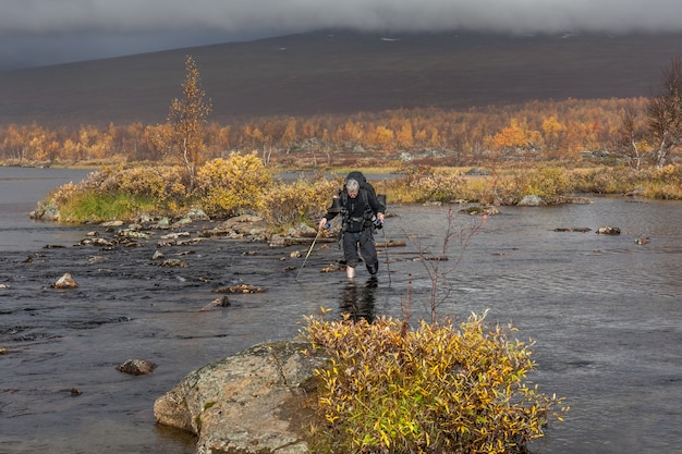 Hiker with backpack crosses cold creek. on a trekking tour in Sarek