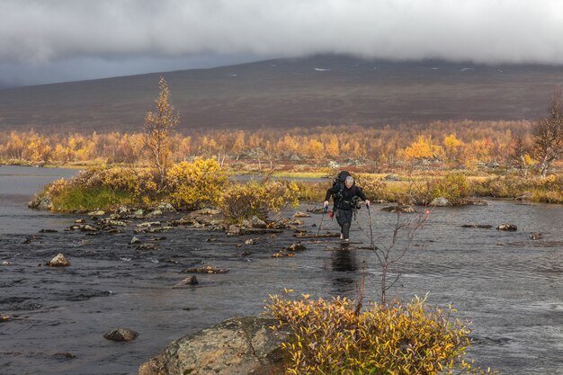 Hiker with backpack crosses cold creek. on a trekking tour in Sarek