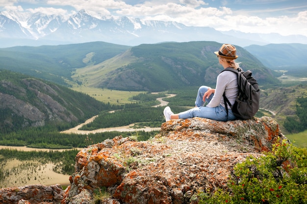 Hiker with backpack relaxing on top of a mountain and enjoying valley view.