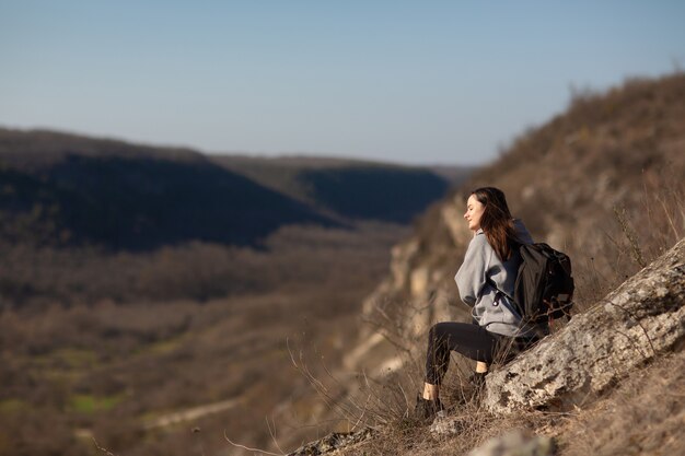 hiker with backpack sitting on the cliff edge and enjoying valley view during trekking route