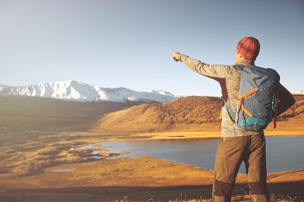 Hiker with backpack standing on top of a mountain with raised hands and enjoying sunrise