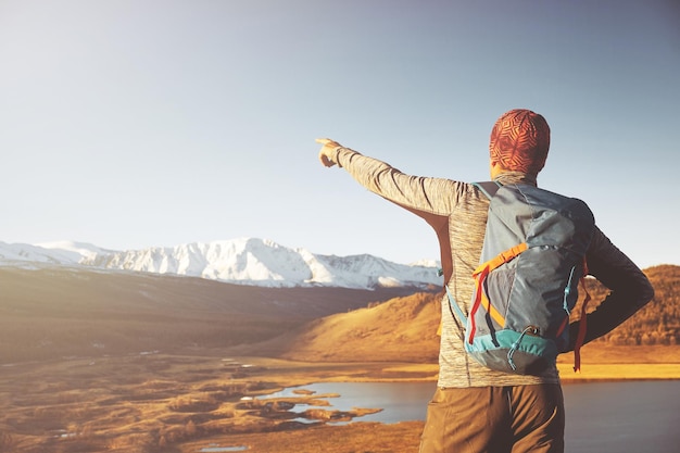 Hiker with backpack standing on top of a mountain with raised hands and enjoying sunrise