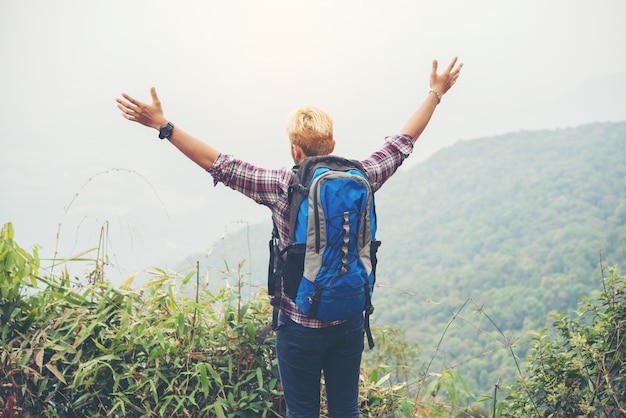 Hiker with backpack standing on top of a mountain with raised hands.