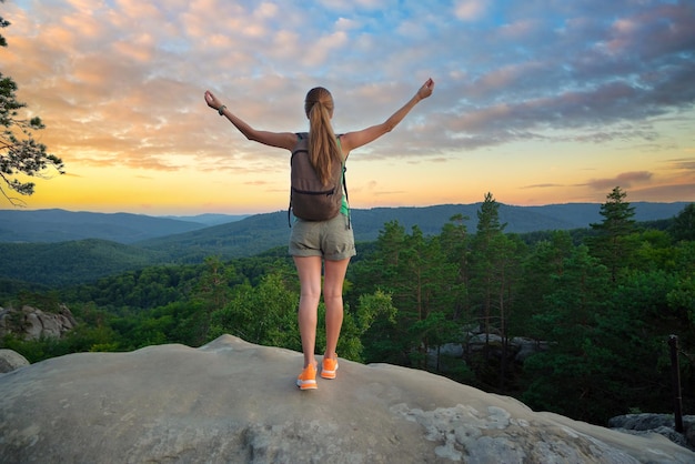 Hiker woman relaxing on mountain footpath raising up hands enjoying evening nature during travel on wilderness trail Lonely female traveler traversing high hilltop route Healthy lifestyle concept