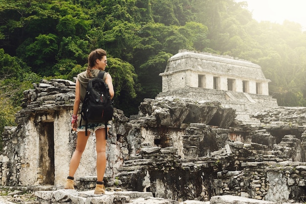 Hiker woman with a backpack looking at ancient Mayan ruins