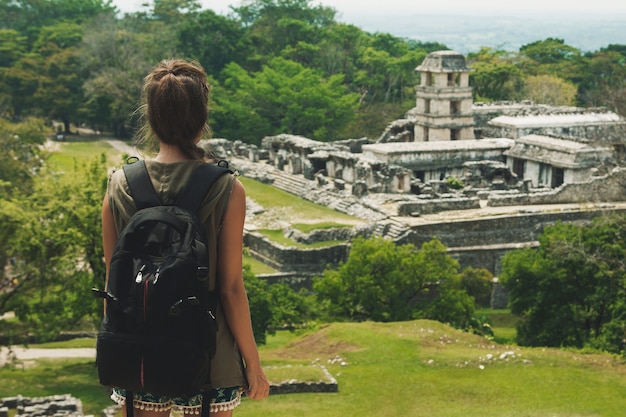 Hiker woman with a backpack looking at ancient Mayan ruins