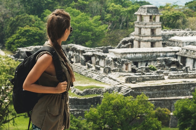 Hiker woman with a backpack looking at ancient Mayan ruins