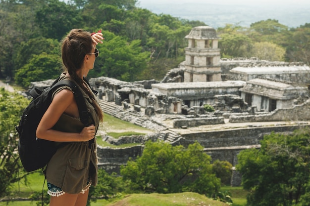 Hiker woman with a backpack looking at ancient Mayan ruins