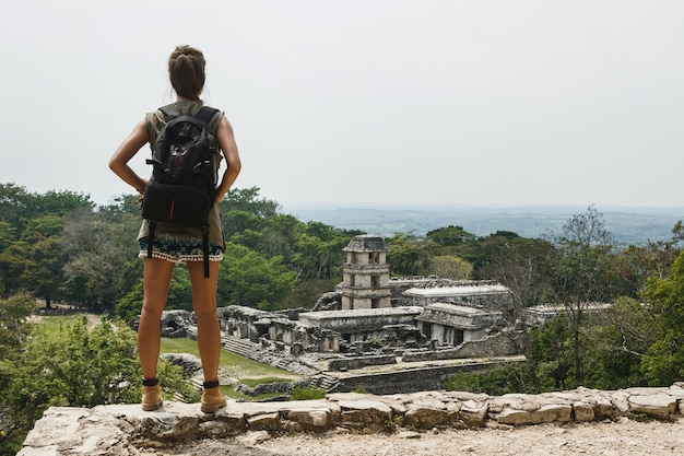 Hiker woman with a backpack looking at ancient Mayan ruins