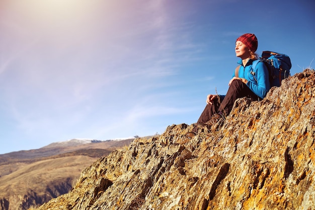 Hiker woman with backpack sitting on rock of a mountain and enjoying sunrise