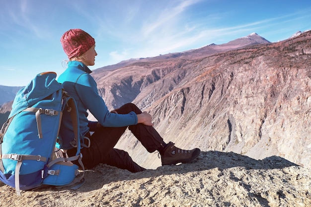 Hiker woman with backpack sitting on rock of a mountain