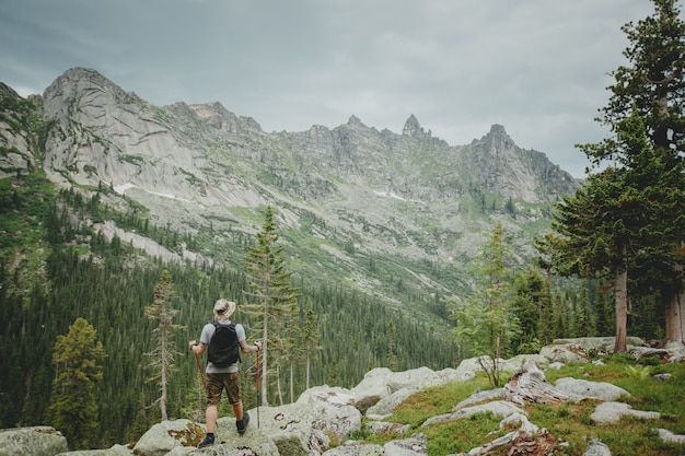 Hiker young man with backpack and trekking of cliff and looking at the mountains in summer outdoor