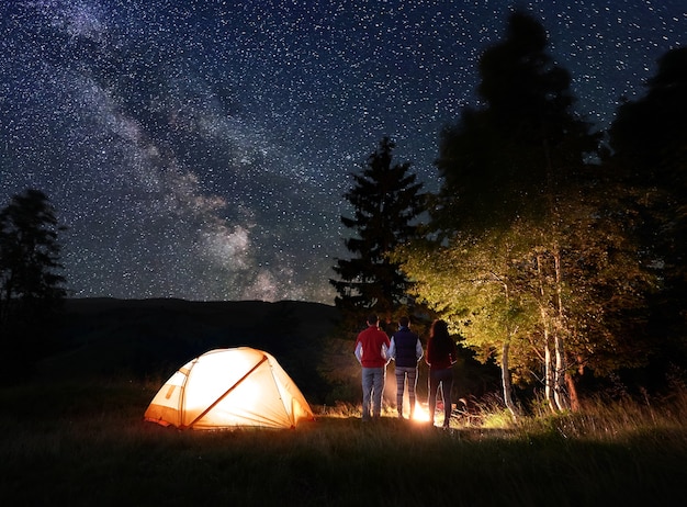 Hikers near campfire and tourist tent at night