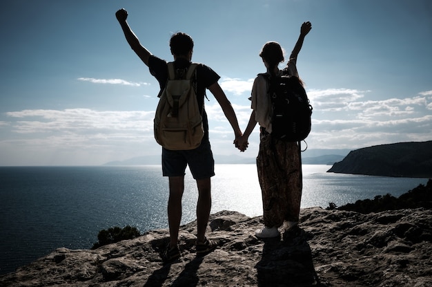 Hikers with backpack standing on top of a mountain with raised hands and enjoying view. team work, man and woman