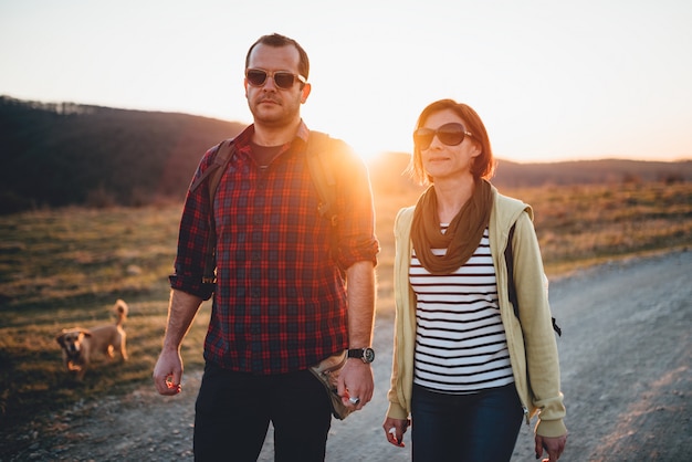 Hiking couple with dog on a dirt road during sunset