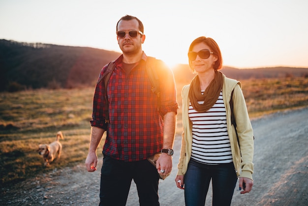 Hiking couple with dog on a dirt road during sunset