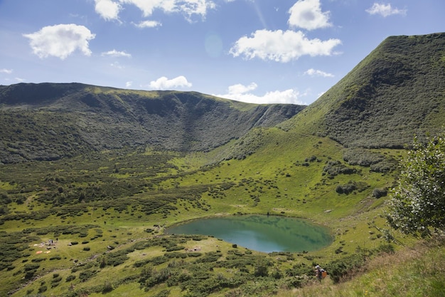 A hiking girl looks at the bowl of a mountain lake surrounded by forests and peaks