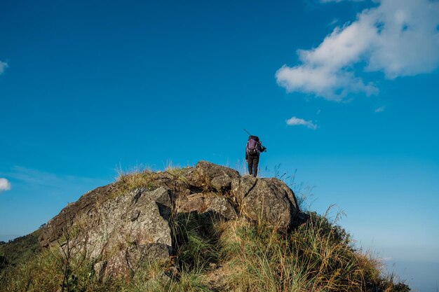 Hiking girl standing with his back on the top of a tall rock beautiful blue sky