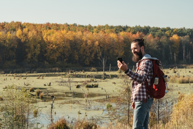 Hiking tourism Side view of man using phone to share nature selfie  swamp and fall forest landscape