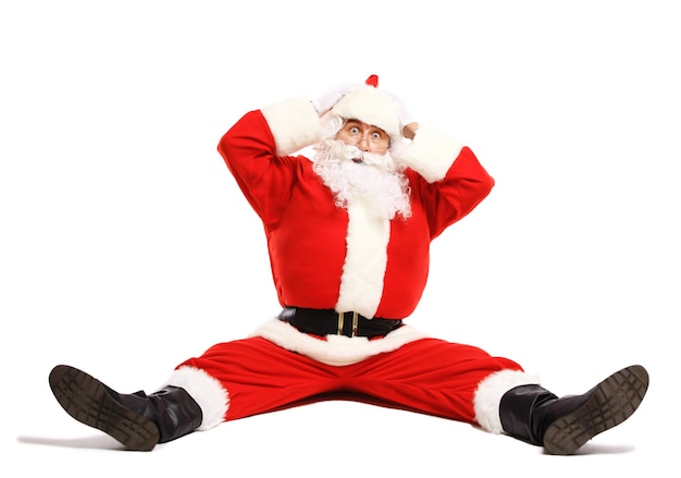 Photo hilarious and funny santa claus confused while sitting on a white surface full length