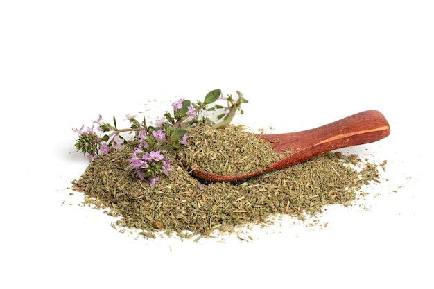 A hill of dried thyme grass with a wooden spoon and a flowering branch of a medicinal thyme plant on a white background