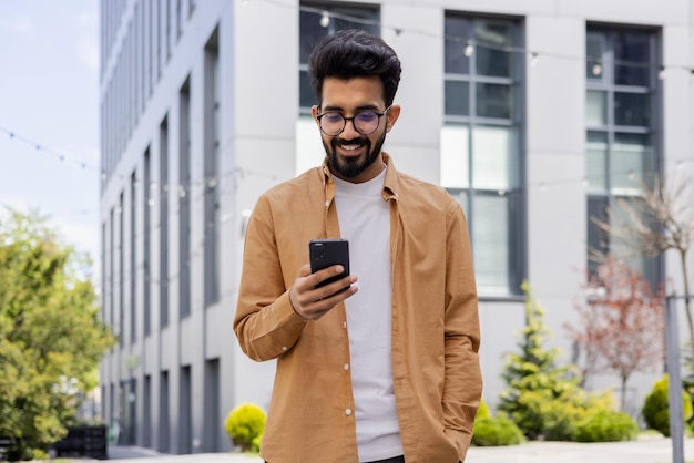 Hindu businessman in casual shirt walking near office building from outside man smiling and using