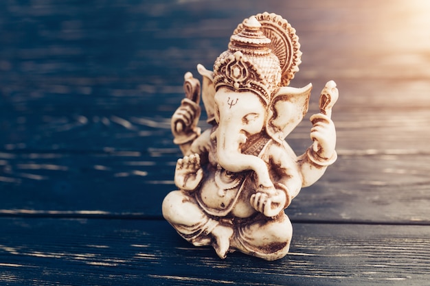 Hindu god Ganesh on black background. Statue on wooden table