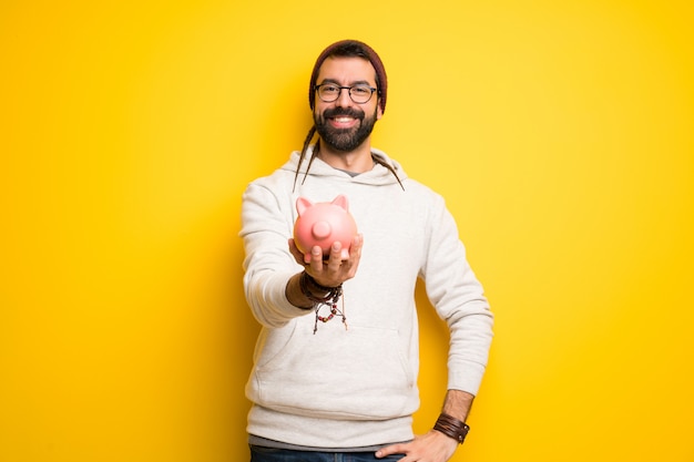 Hippie man with dreadlocks holding a piggybank