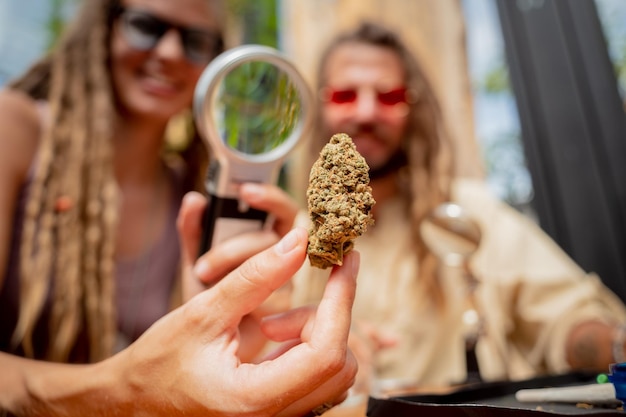 Photo hippie style couple examines under a magnifying glass the joints and buds of medical marijuana