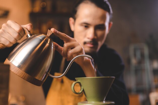 Hipster barista pouring a hot water to making coffee with drip or filter style in cafe slow brew for caffeine aroma beverage drink in cup fresh black coffee and espresso for breakfast