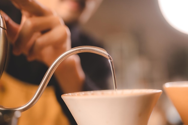 Hipster barista pouring a hot water to making coffee with drip or filter style in cafe slow brew for caffeine aroma beverage drink in cup fresh black coffee and espresso for breakfast