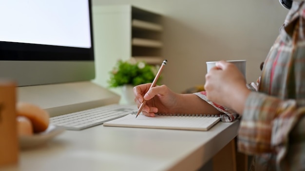 A hipster female in a flannel shirt writing something in her notebook and sipping coffee