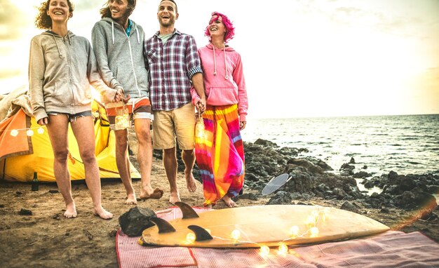 Hipster friends having fun walking with led neon lanterns at beach camping party