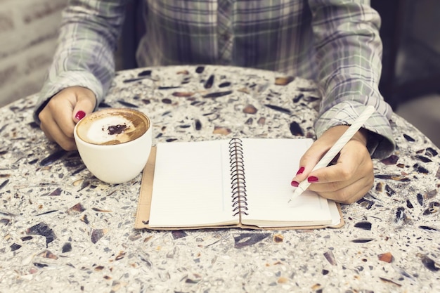 Hipster girl making notes in a diary and drinking coffee