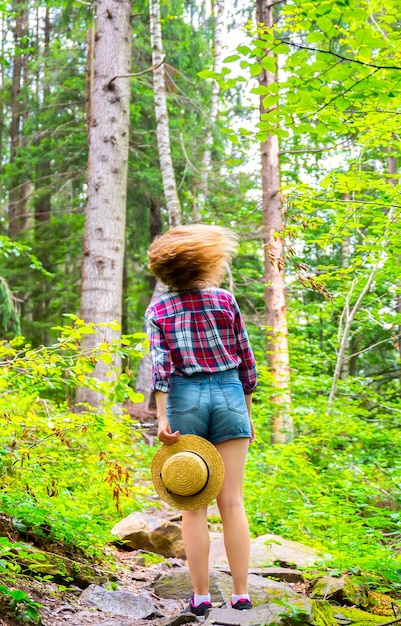 Hipster girl in the mountains. Stylish woman in straw hat and checkered shirt in forest. Wanderlust concept. Freedom and psychology concept. Beautiful nature.