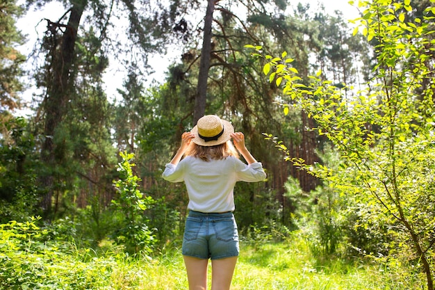 Hipster girl in straw hat standing in the forest. Wanderlust concept. Travelling ideas. Beautiful woman in the nature. Summer vibes.