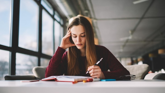 hipster girl study at school cafeteria while reading literature and writing main theses in notebook