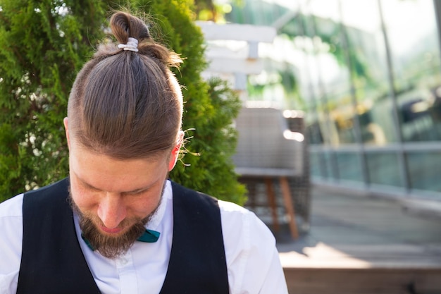 Hipster hairstyle on a young bearded man in a suit sitting in a street cafe