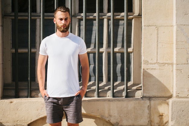 Hipster handsome male model with beard wearing white blank t-shirt with space for your logo or design in casual urban style