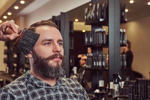 Hipster man in a barber shop. Professional hairdresser uses a brush, almost finished hairstyle.