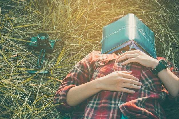 hipster man lying down on grassland napping tired after reading book with nature around ou