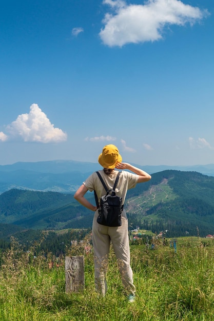 Hipster traveler in hat and backpack resting in nature A tourist girl looks at the panorama