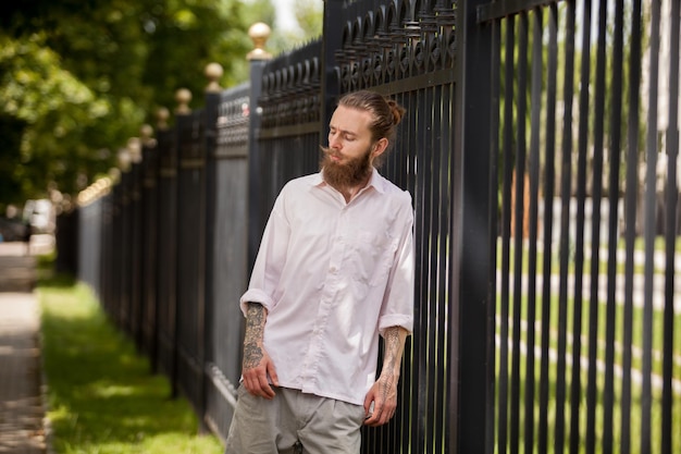 Hipster with long beard posing next to a fence outside in the city. Style and diversity