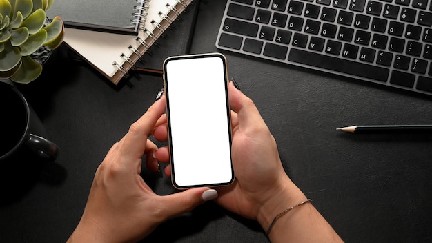 Hipster woman holding a smartphone blank screen mockup over modern black worktable background